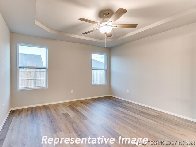 empty room with a raised ceiling, ceiling fan, and light hardwood / wood-style flooring