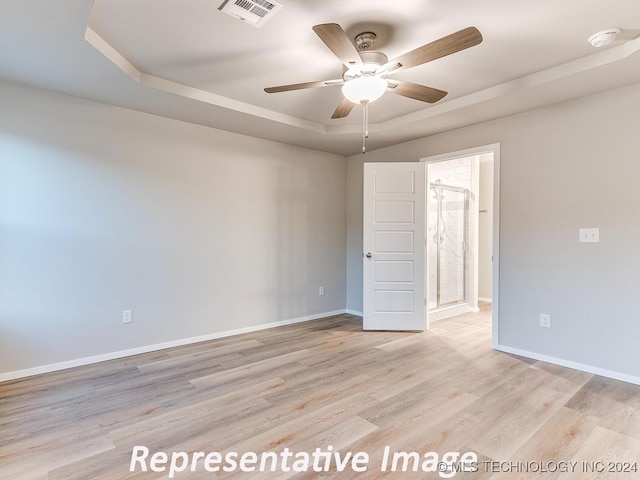 unfurnished room featuring a tray ceiling, ceiling fan, and light hardwood / wood-style floors