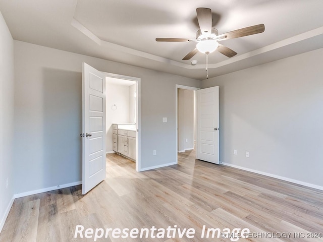 unfurnished bedroom with a tray ceiling, ceiling fan, ensuite bathroom, and light hardwood / wood-style floors