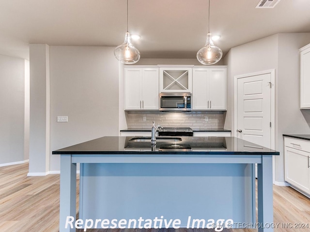 kitchen with light wood-type flooring, a center island with sink, and white cabinetry