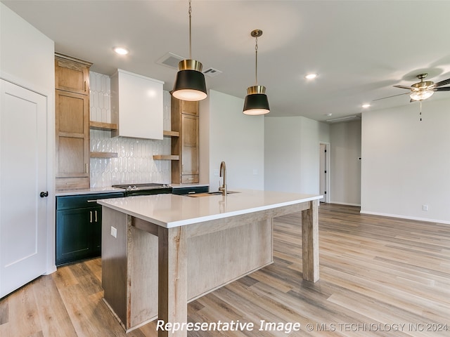 kitchen featuring ceiling fan, light hardwood / wood-style floors, hanging light fixtures, and an island with sink