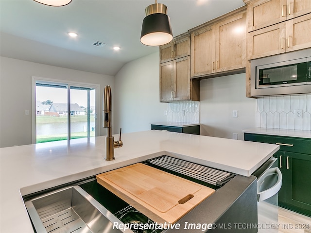 kitchen featuring decorative backsplash, light brown cabinetry, vaulted ceiling, a center island, and stainless steel microwave