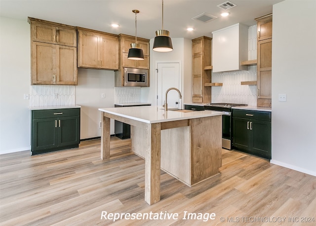 kitchen featuring hanging light fixtures, sink, light wood-type flooring, an island with sink, and appliances with stainless steel finishes