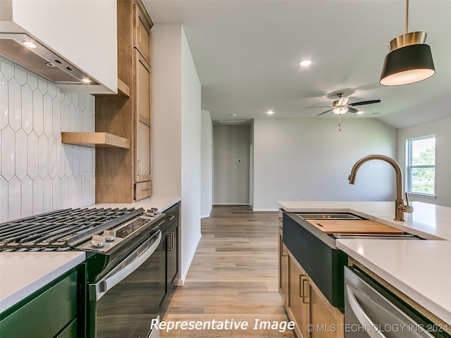 kitchen featuring light wood-type flooring, stainless steel appliances, vaulted ceiling, wall chimney range hood, and pendant lighting