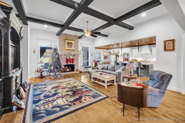 living room featuring beamed ceiling, ceiling fan, light wood-type flooring, and a fireplace