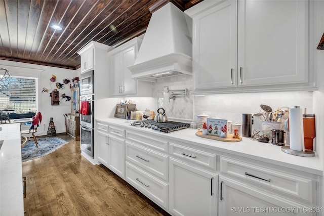 kitchen featuring wood ceiling, custom exhaust hood, built in microwave, wood-type flooring, and white cabinetry