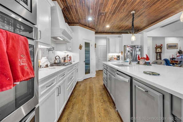 kitchen with custom exhaust hood, white cabinets, hanging light fixtures, wood ceiling, and stainless steel appliances