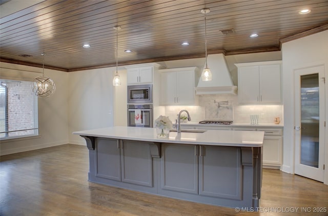 kitchen featuring a spacious island, custom exhaust hood, white cabinetry, decorative light fixtures, and appliances with stainless steel finishes