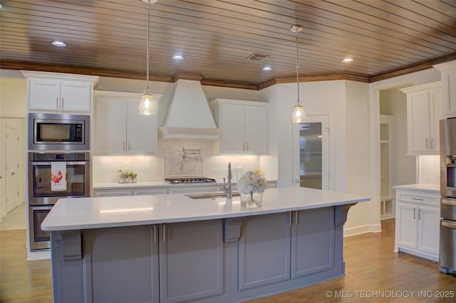 kitchen with white cabinetry, decorative light fixtures, custom exhaust hood, and a center island with sink