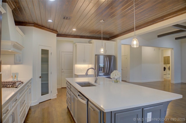 kitchen with sink, custom exhaust hood, separate washer and dryer, appliances with stainless steel finishes, and an island with sink