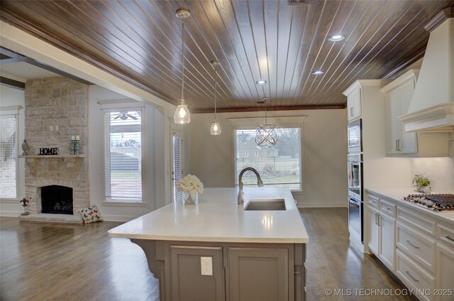 kitchen with hanging light fixtures, stainless steel appliances, custom range hood, an island with sink, and white cabinets