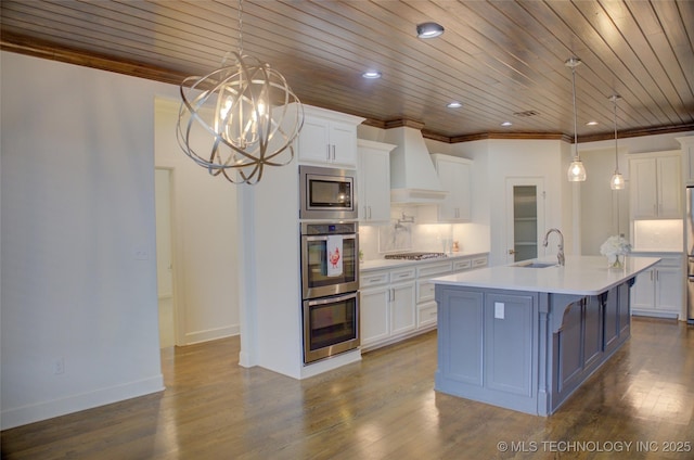 kitchen featuring sink, white cabinets, custom exhaust hood, hanging light fixtures, and a kitchen island with sink