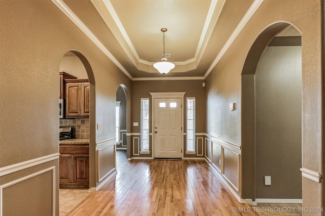 foyer featuring a tray ceiling, crown molding, and light hardwood / wood-style floors