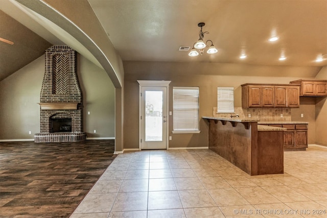 kitchen with light stone countertops, a kitchen breakfast bar, kitchen peninsula, an inviting chandelier, and a fireplace