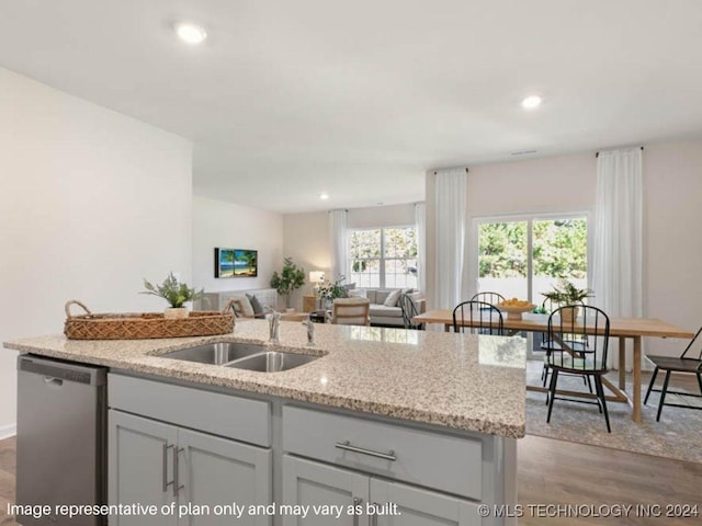 kitchen featuring light stone countertops, stainless steel dishwasher, sink, a center island with sink, and dark hardwood / wood-style floors