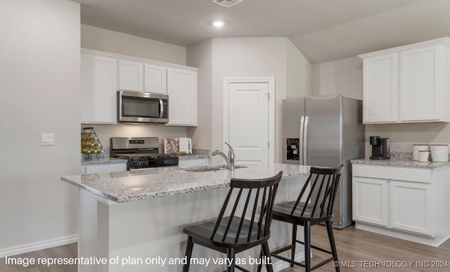 kitchen featuring a breakfast bar area, white cabinets, stainless steel appliances, light stone countertops, and light hardwood / wood-style flooring