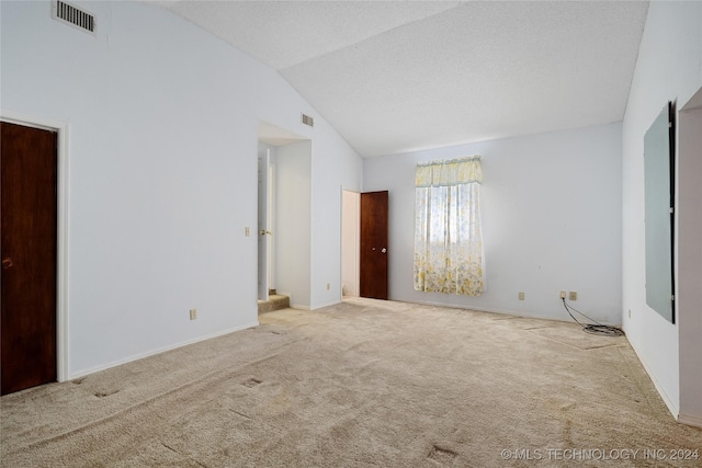 spare room featuring a textured ceiling, light colored carpet, and lofted ceiling