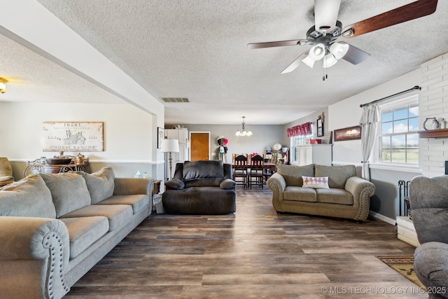 living room featuring dark wood-type flooring, ceiling fan with notable chandelier, and a textured ceiling