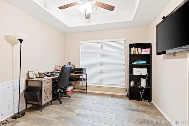 home office with a raised ceiling, light hardwood / wood-style flooring, and ceiling fan