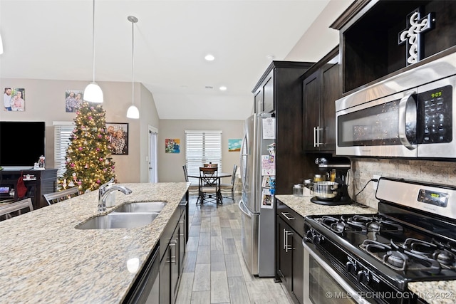 kitchen with light stone countertops, appliances with stainless steel finishes, light wood-type flooring, sink, and hanging light fixtures