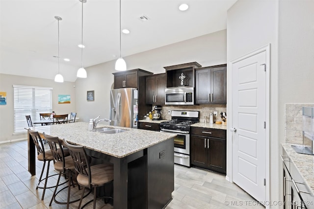 kitchen with sink, hanging light fixtures, stainless steel appliances, an island with sink, and decorative backsplash