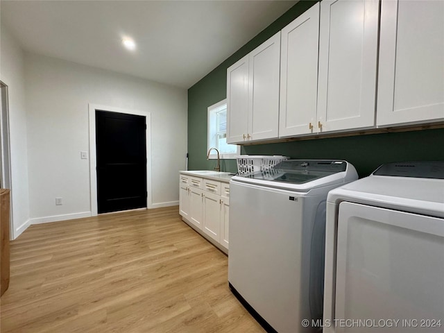 clothes washing area featuring sink, light hardwood / wood-style flooring, cabinets, and washing machine and clothes dryer