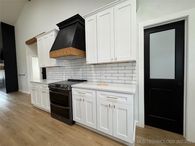 kitchen with premium range hood, white cabinetry, tasteful backsplash, light hardwood / wood-style flooring, and range with two ovens