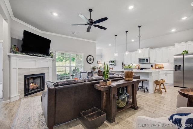 living room with a tile fireplace, light wood-type flooring, ceiling fan, and ornamental molding