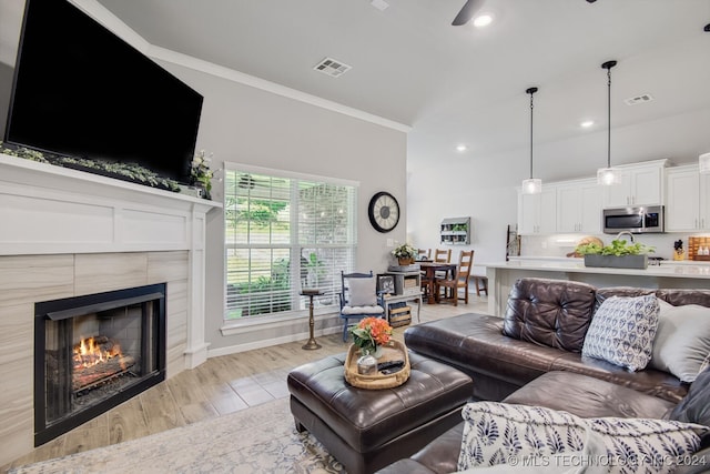 living room featuring a tiled fireplace, crown molding, light hardwood / wood-style flooring, and ceiling fan