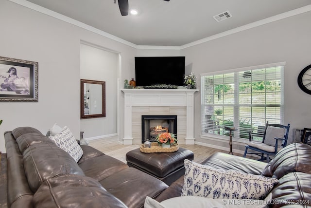 living room with ceiling fan, light wood-type flooring, crown molding, and a tile fireplace