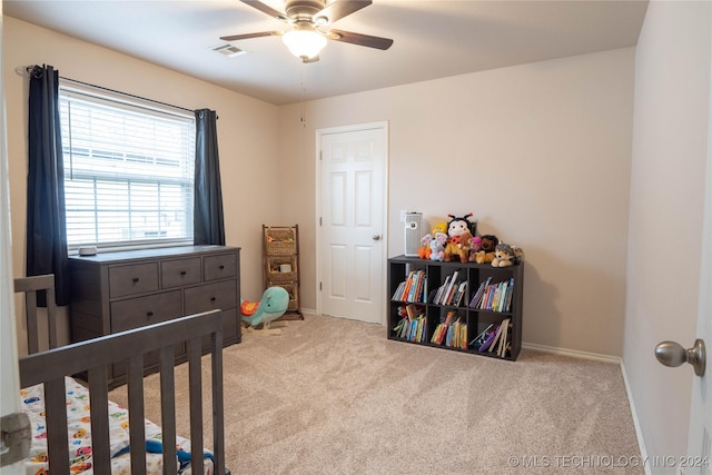 bedroom featuring a crib, light colored carpet, and ceiling fan