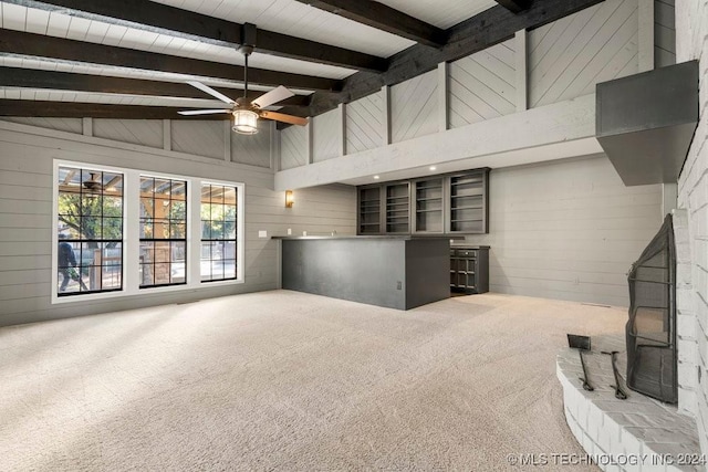 unfurnished living room featuring wood walls, a ceiling fan, beamed ceiling, carpet, and a wood stove