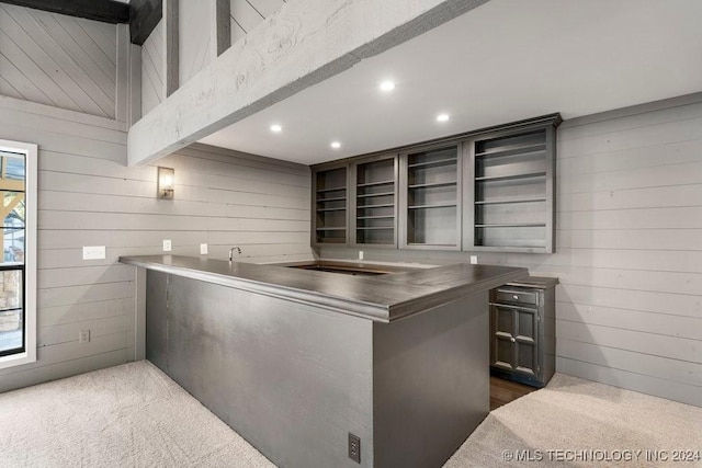 kitchen featuring dark colored carpet, beam ceiling, kitchen peninsula, and wooden walls