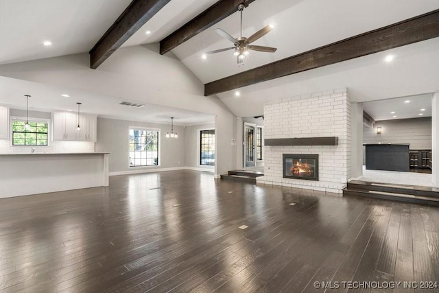 unfurnished living room with lofted ceiling with beams, dark wood-type flooring, visible vents, a ceiling fan, and a brick fireplace