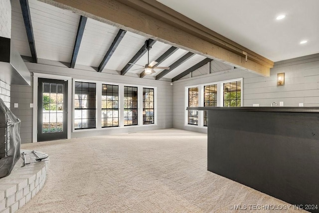 carpeted living area with a healthy amount of sunlight, wood walls, ceiling fan, and lofted ceiling with beams