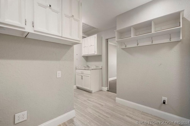 clothes washing area with light wood-type flooring, a textured wall, and baseboards