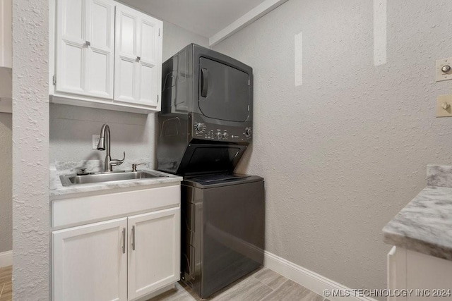 washroom featuring cabinets, stacked washing maching and dryer, sink, and light hardwood / wood-style flooring