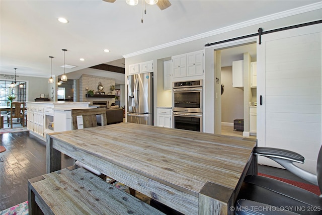 kitchen with crown molding, stainless steel appliances, light countertops, a barn door, and white cabinetry