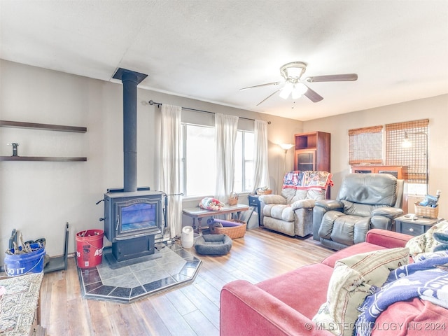 living area with ceiling fan, a textured ceiling, wood finished floors, and a wood stove