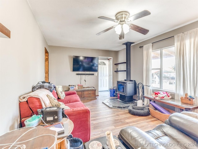 living area featuring a wood stove, light wood-style floors, and a ceiling fan