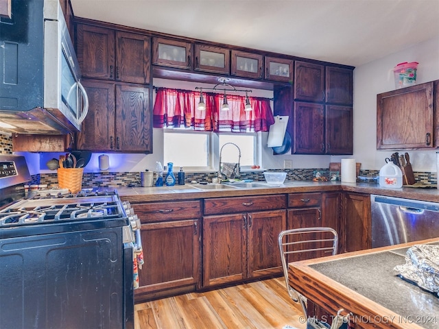 kitchen featuring stainless steel appliances, light wood finished floors, a sink, and glass insert cabinets