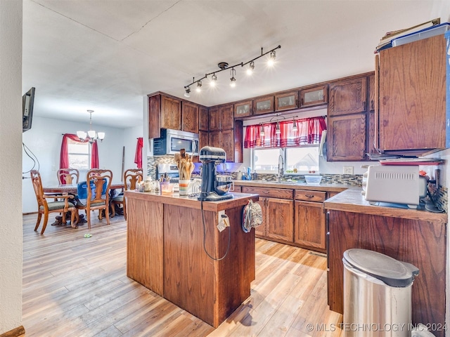 kitchen featuring light wood-style flooring, glass insert cabinets, hanging light fixtures, stainless steel appliances, and a sink