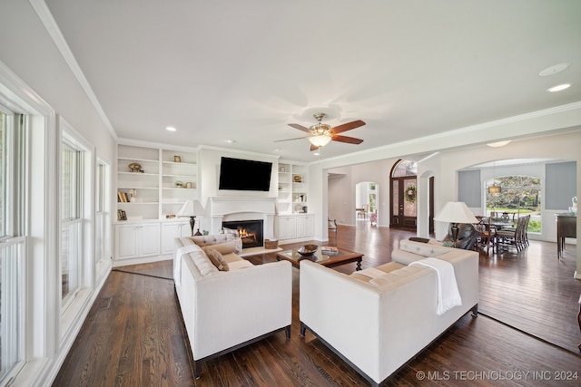 living room with crown molding, ceiling fan, dark wood-type flooring, and built in shelves