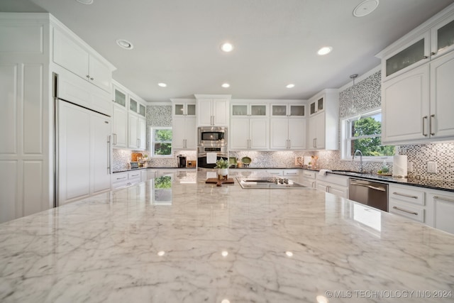 kitchen featuring a wealth of natural light, built in appliances, white cabinets, and dark stone counters