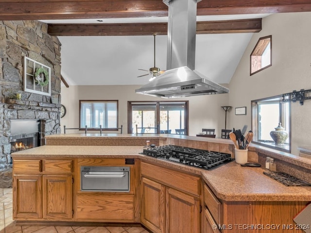 kitchen with stainless steel gas stovetop, vaulted ceiling with beams, ceiling fan, a fireplace, and island range hood