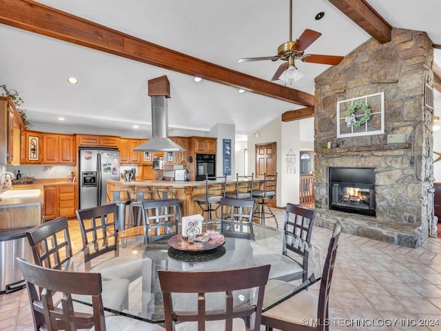 dining area with a fireplace, lofted ceiling with beams, ceiling fan, and sink