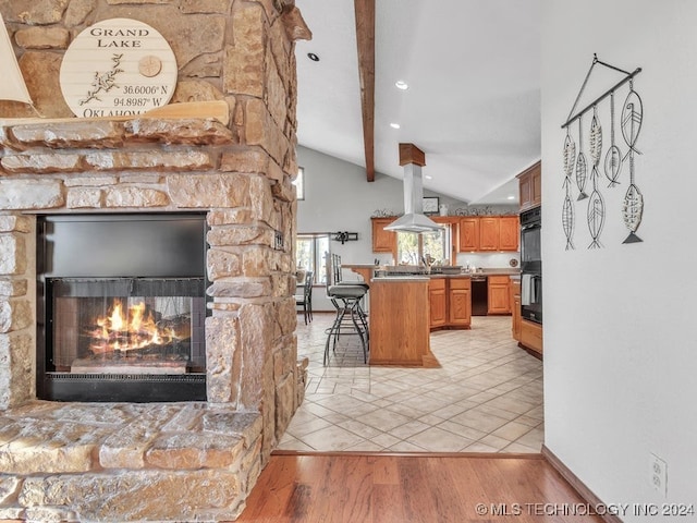 kitchen featuring island exhaust hood, a breakfast bar, light hardwood / wood-style flooring, vaulted ceiling with beams, and a stone fireplace