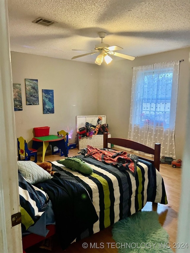 bedroom with ceiling fan, wood-type flooring, and a textured ceiling