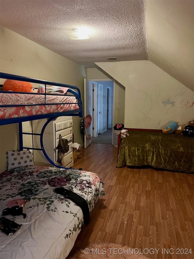 bedroom with vaulted ceiling, wood-type flooring, and a textured ceiling