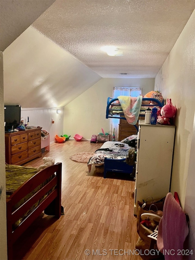 bedroom with a textured ceiling, light hardwood / wood-style floors, and vaulted ceiling